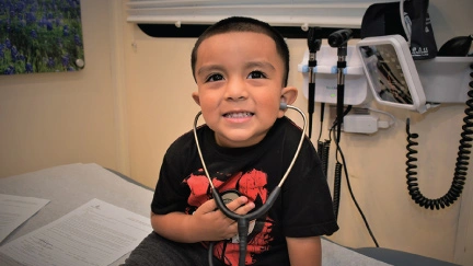 young boy sitting on medical examination table with stethoscope in his ears and holding receiver to his chest, smiling
